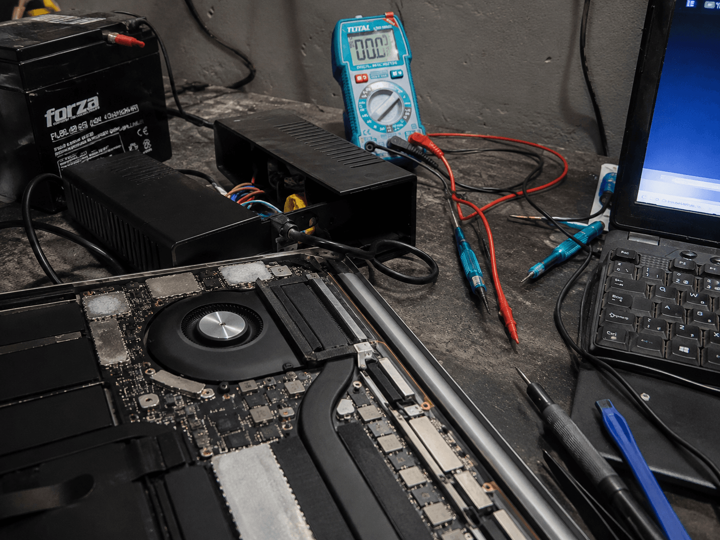 Mesa de diagnóstico técnico con computadora abierta, multímetro y herramientas de reparación